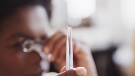 trabajadora biracial inspeccionando joyas con lupa en el estudio en cámara lenta