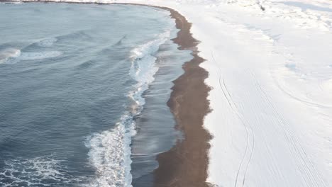 snowy coastline at sandvik beach in iceland with waves, aerial