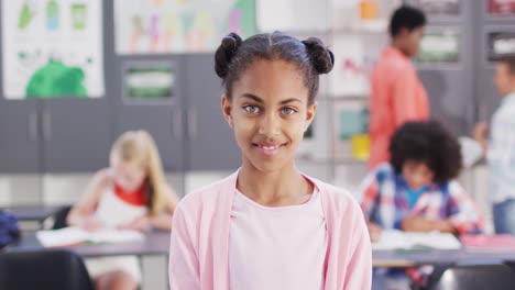 portrait of smiling biracial schoolgirl in classroom with diverse class and teacher behind