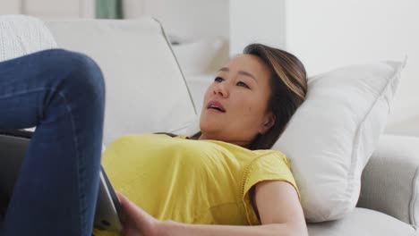 happy asian woman lying on sofa, resting with laptop at home