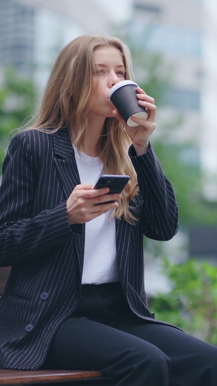 Ung forretningskvinde bruger smartphone og drikker kaffe på en parkbænk