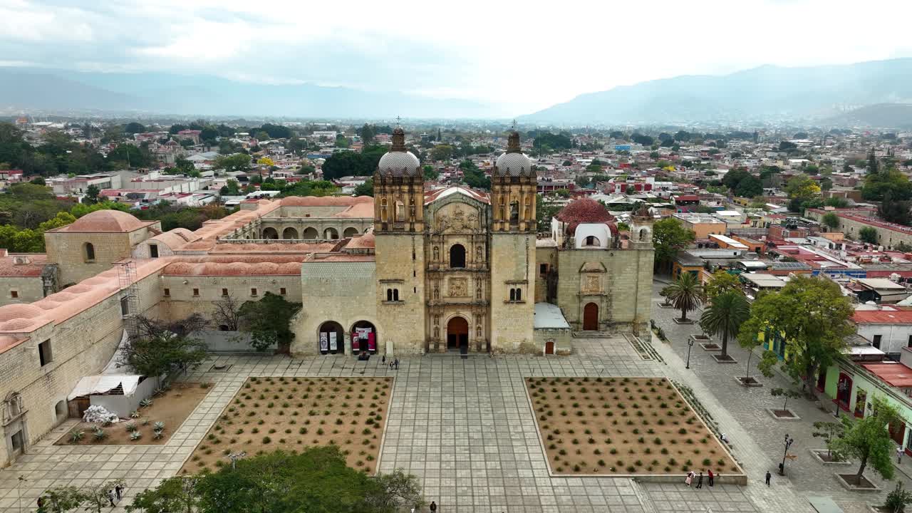 Crane-up or jib move revealing the Templo de Santo Domingo de Guzmán and Oaxaca City beyond. Colonial facade, plaza, and urban backdrop—clean destination establishing shot