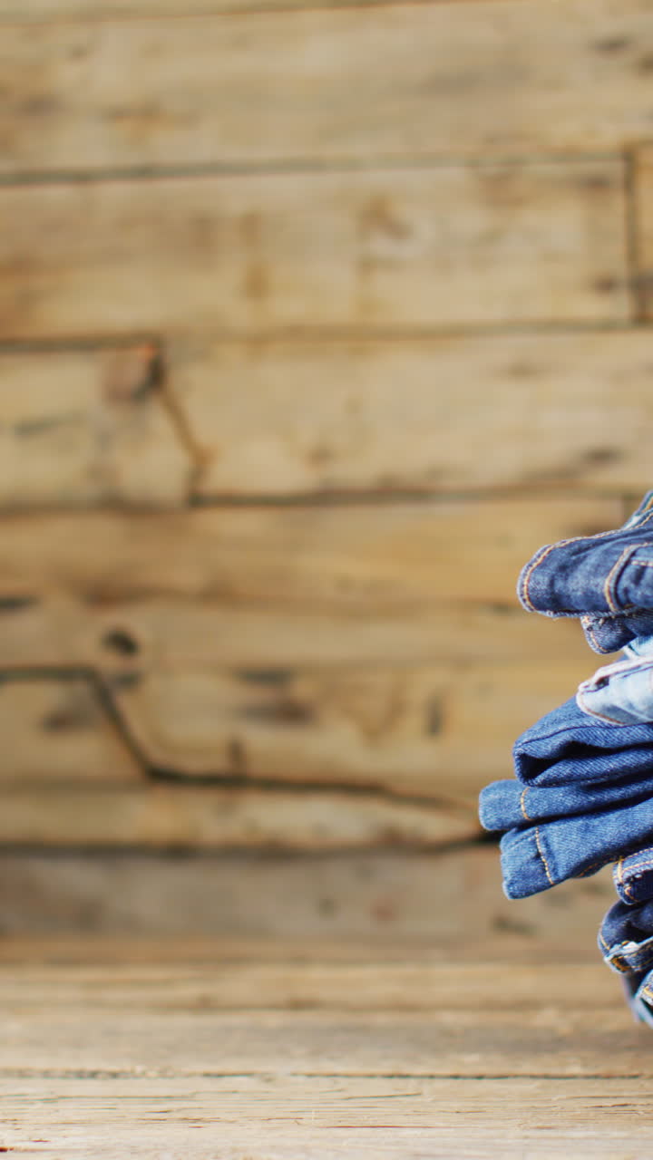 Vertical video of folded jeans with different shades on wooden background with copy space