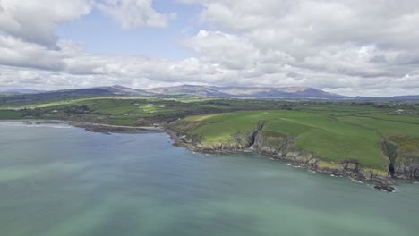 Antena-Acercándose-A-La-Costa-De-Waterford-Con-Las-Montañas-Comeragh-Al-Fondo-En-Un-Cálido-Día-De-Primavera