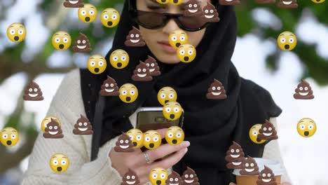 animation of od falling emojis over woman in hijab using smartphone