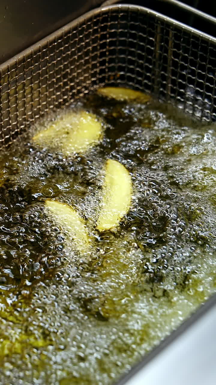 Cooking in deep fryer. Golden potato frying in a hot boiling oil in the restaurant. Crispy vegetables in deep fryer. Unhealthy food. Vertical video
