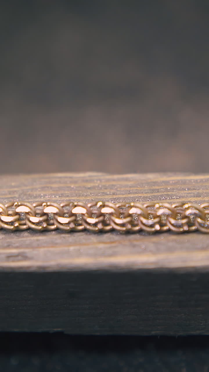 CU shot: young jeweler polishes shining gold chain with rasp on wooden gutter at dark table in workshop extreme closeup