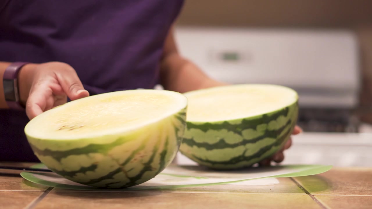 Black woman separating the halves of a sliced yellow watermelon, Slowmo Closeup