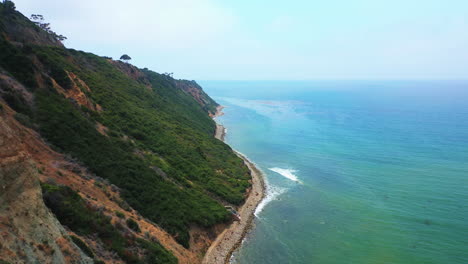 waves breaking against a rocky shoreline below the rugged terrain of palos verdes, california - pull back aerial view