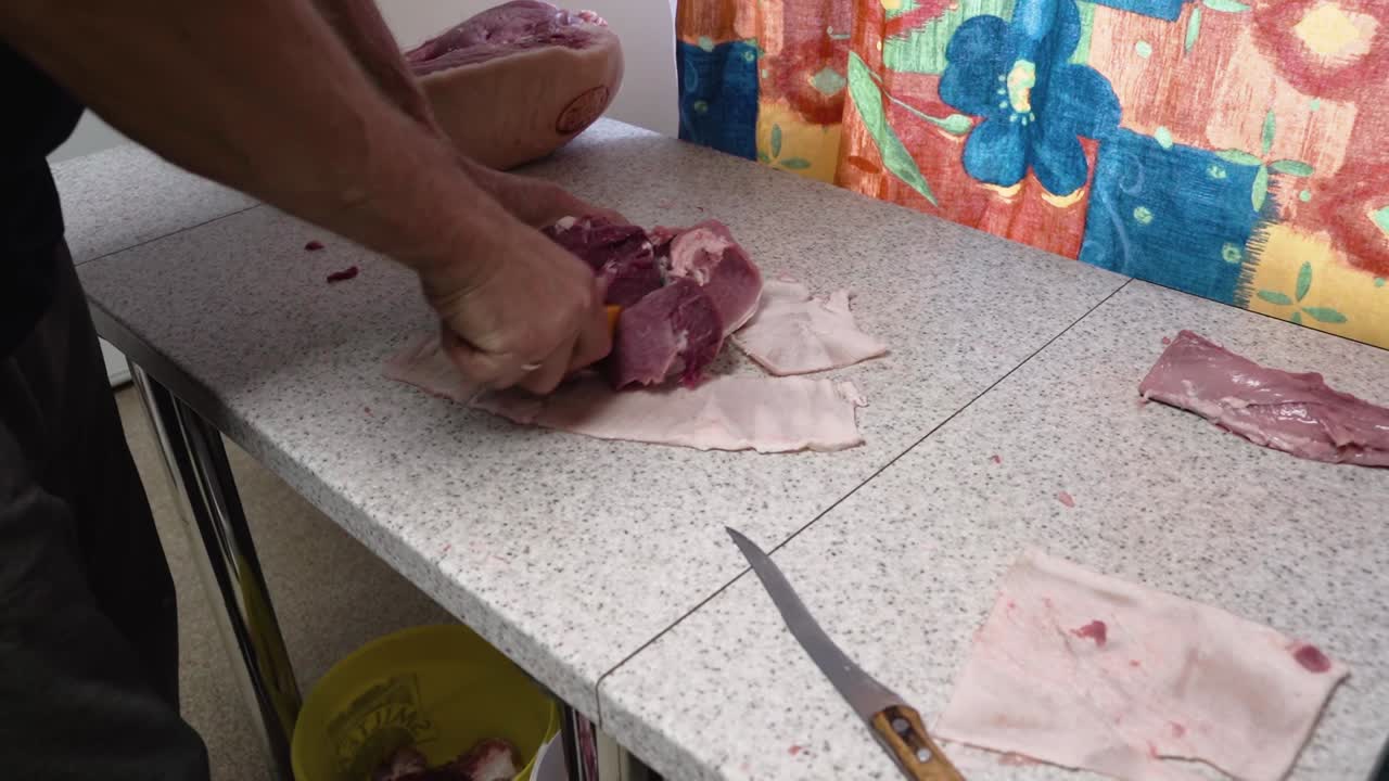 persona cortando carne de cerdo cruda en la mesa de la cocina con un cuchillo afilado