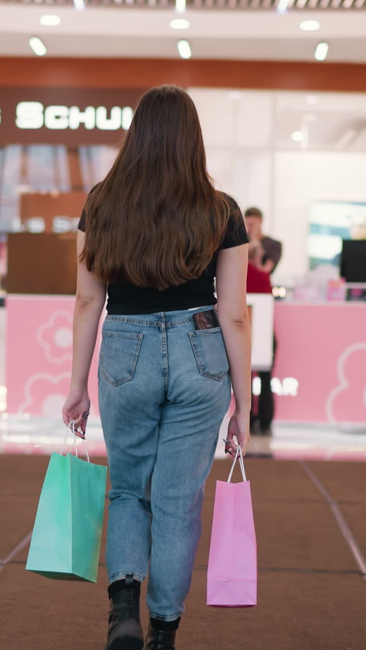 vista trasera de una joven con bolsas de compras bajando de la escalera mecánica en el centro comercial, un niño pasando en el fondo, luces vibrantes y reflejos del techo decorativo por encima