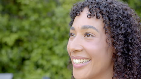 smiling woman with curly hair enjoying outdoor time in garden setting, copy space