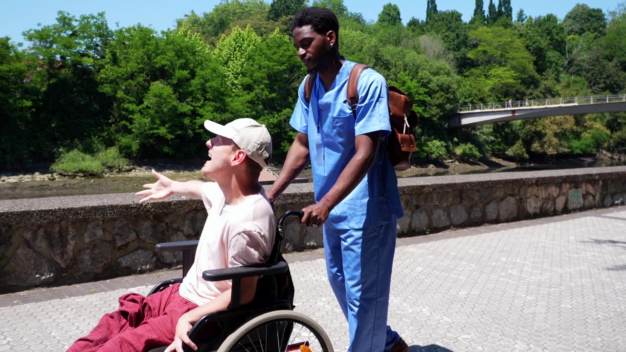Aidant poussant un jeune homme en fauteuil roulant le long d'une berge
