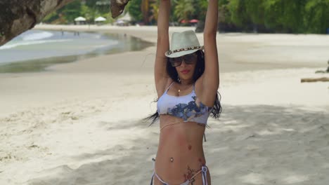 on the white sands of a tropical caribbean beach, a girl in a bikini relishes the sun while swinging from a tree branch