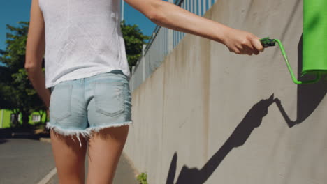 joven artista que pinta una pared con pintura verde caminando por la calle de la ciudad mujer independiente que disfruta de la expresión artística con el arte de graffiti urbano 4k