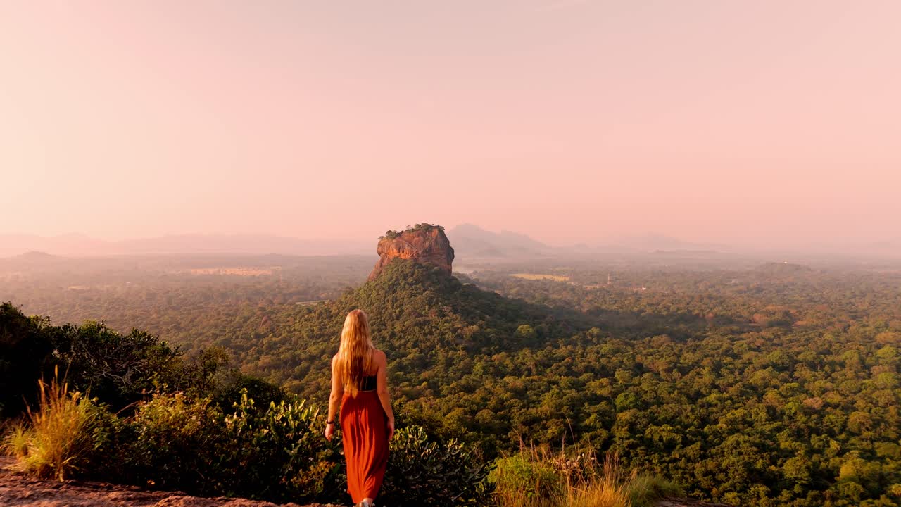 A young woman runs across the summit of Pidurangala Rock to catch the magical sunrise over Sigiriya Rock.