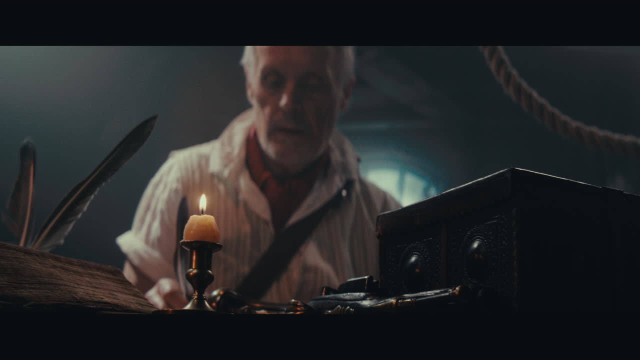 An old captain sits writes a letter inside the sailing ship cabin