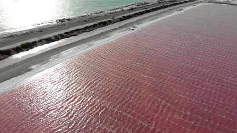 Aerial-reveal-view-of-the-pink-salt-flats-of-Bonaire-contrasted-with-the-turquoise-ocean-along-the-road