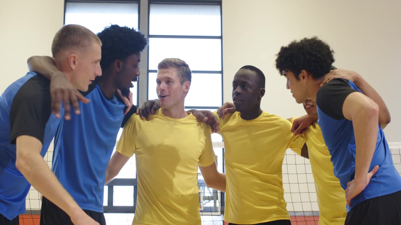 Diverse male players walking center court, linking arms, stacking hands by volleyball net for cheer