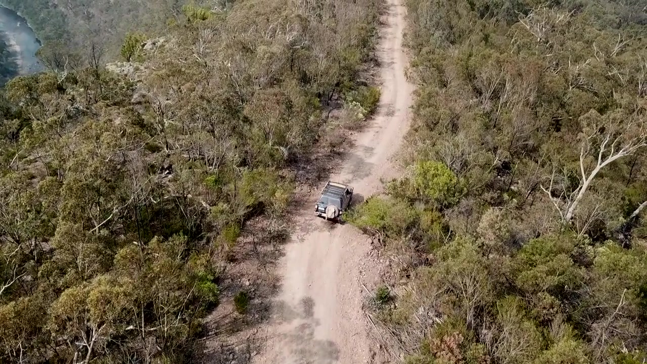 Smooth drone follow shoot for an off road car in motion in a road between green trees over a high mountain during the day