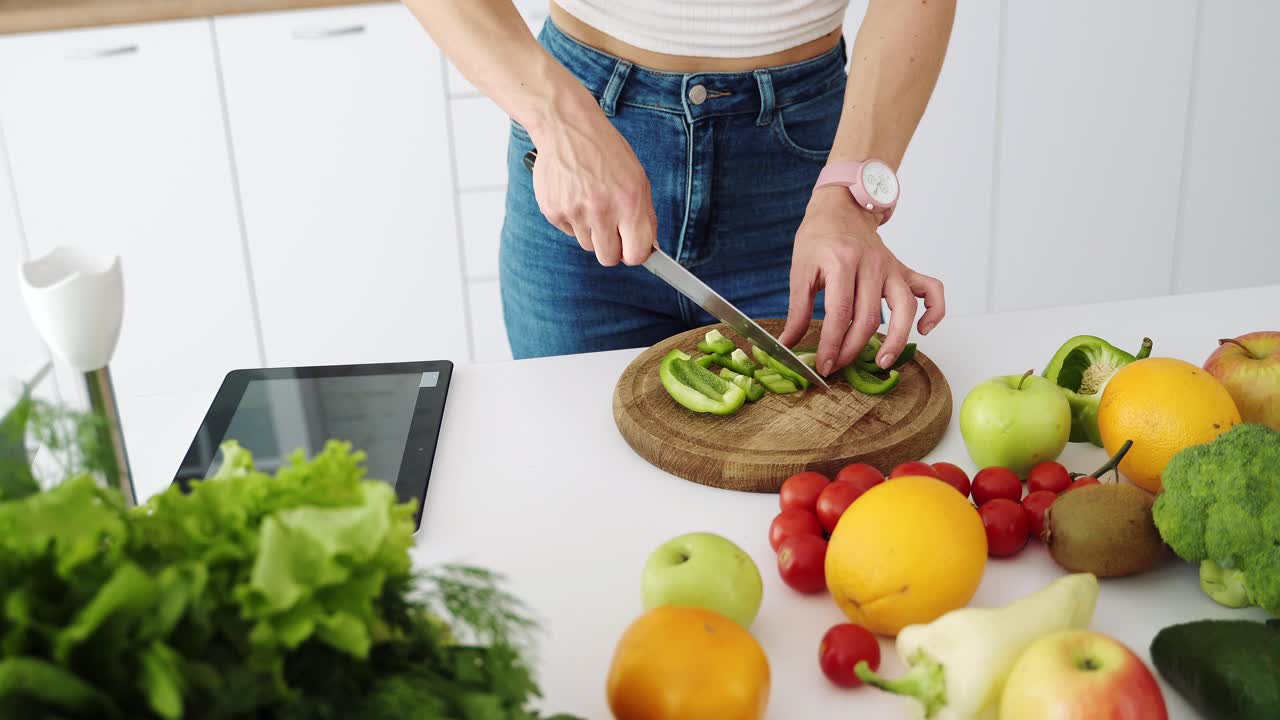 The girl cuts with a knife a green bell pepper. Table with vegetables and fruits for a healthy diet