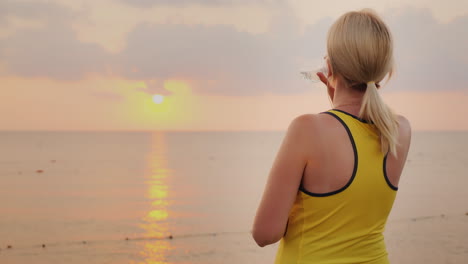 fitness woman is drinking water from a bottle it stands in a picturesque place by the sea at dawn re