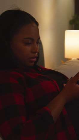 mujer usando un teléfono inteligente en un sofá por la noche