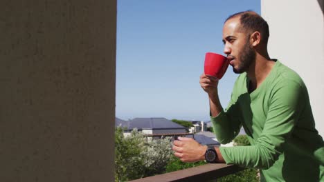 mixed race man drinking coffee on balcony in the sun