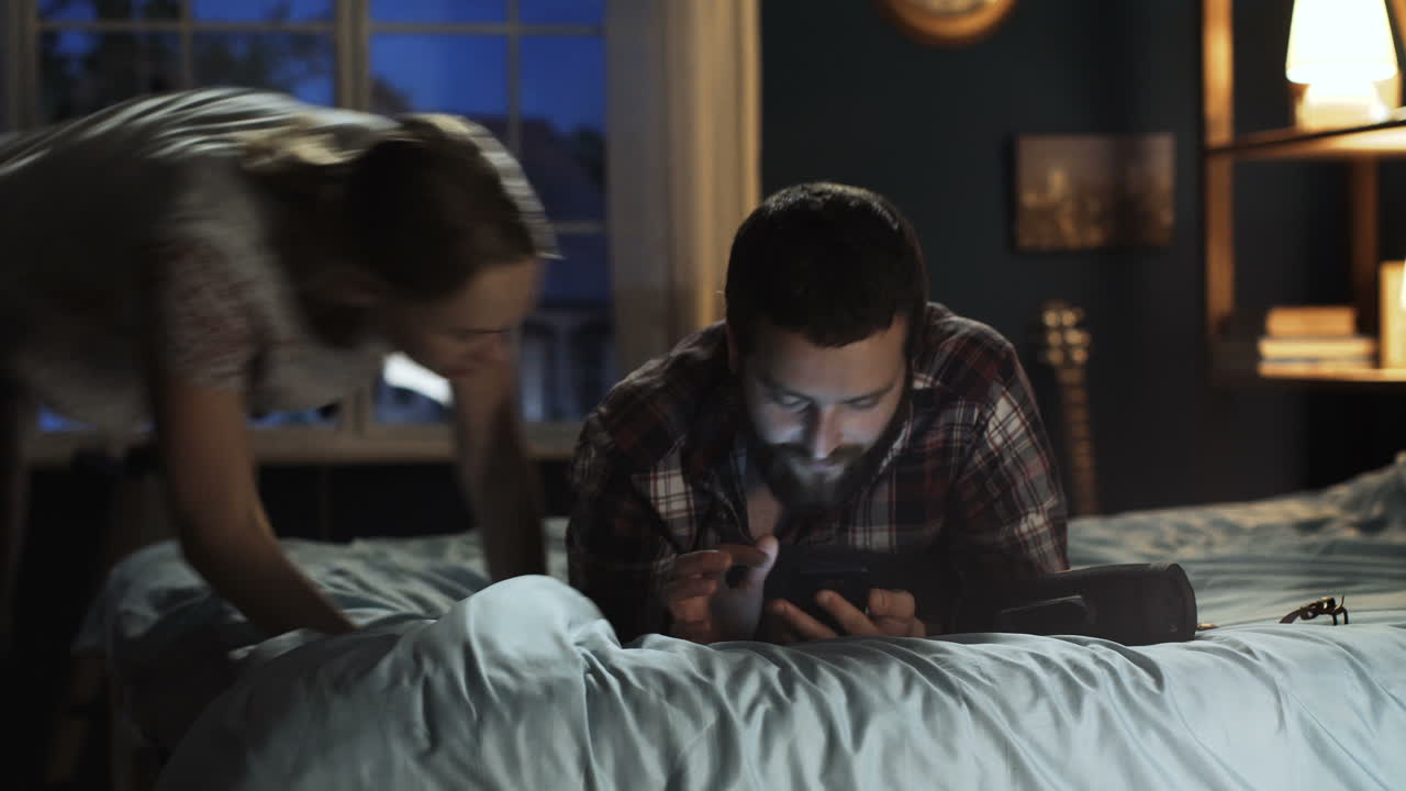 Couple Sharing a Mobile Phone in Bed at Night