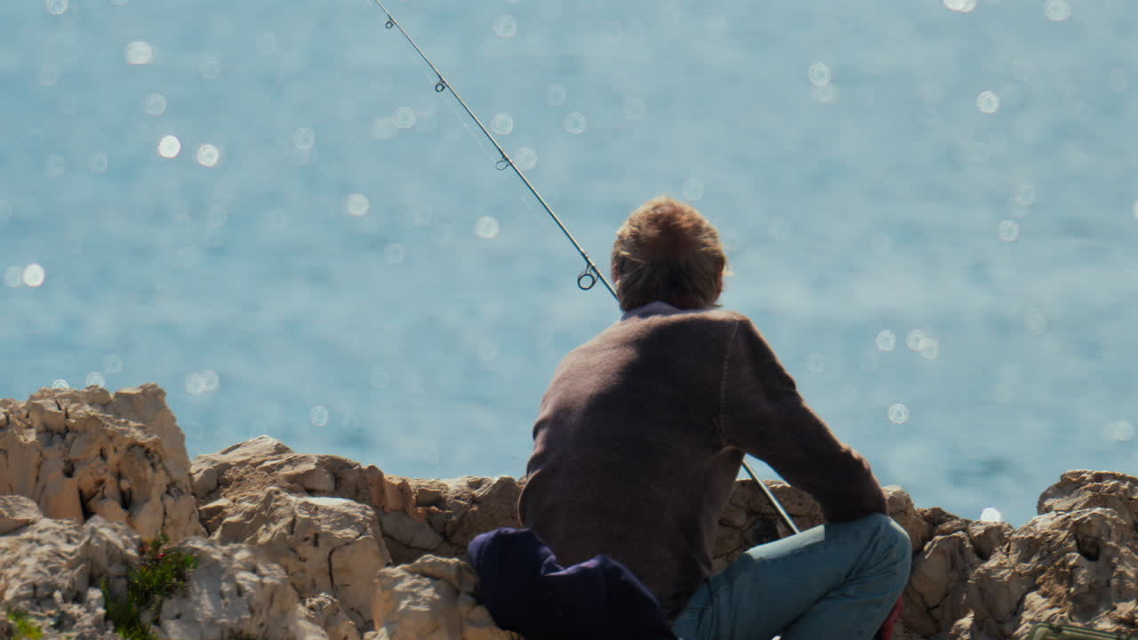 View of an old man fishing in the sea on a sunny day