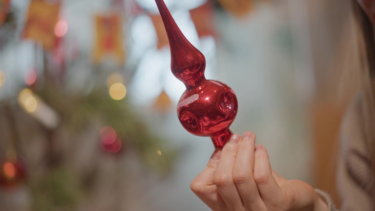 Donna allegra si prepara ad appendere un ornamento. Donna felice tiene delicatamente una decorazione rossa vicino all'albero di Natale. Donna gioiosa offre con cura un ornamento rosso pronto per essere appeso all'albero festivo decorato.
