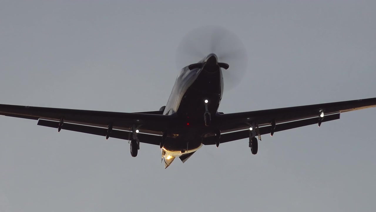 Piccolo aereo a elica in volo con le luci di atterraggio accese al tramonto