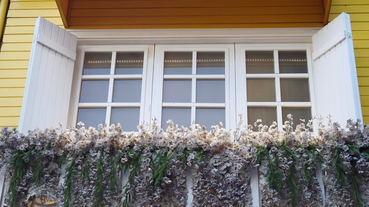 Hvitt vindu med skodder og blomster på en gul vegg