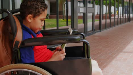 Side view of disabled African American schoolboy using digital tablet in school corridor 4k