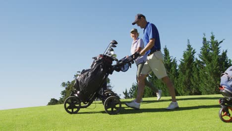 caucasian senior couple walking with their golf bags at golf course on a bright sunny day