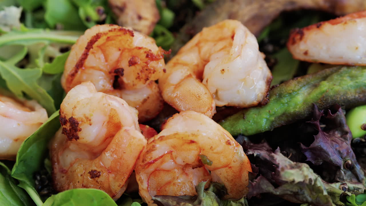 Close up of a fresh salad topped with grilled shrimp, leafy greens, avocado, and vegetables, perfect for healthy eating