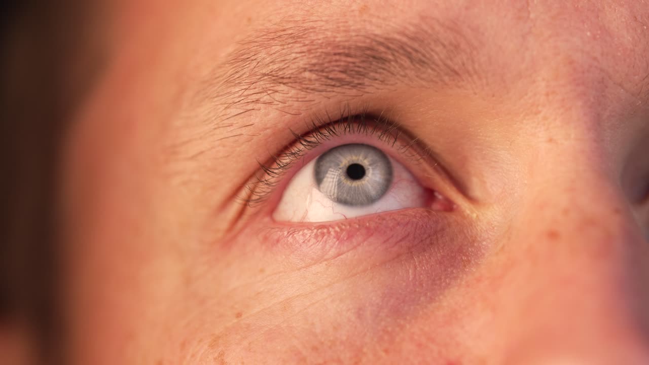 Blue eye captures light while looking up and blinking gently.