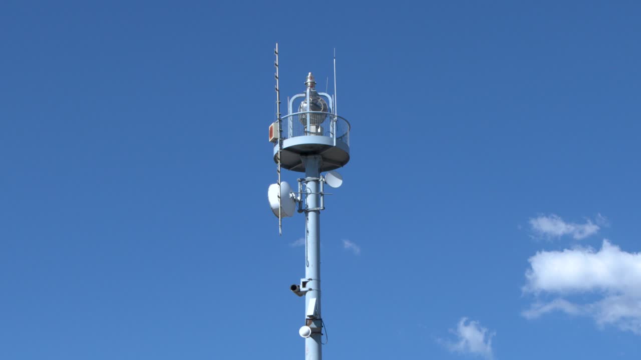 A vertical camera tilt captures a tall metal telecommunication tower against a clear blue sky