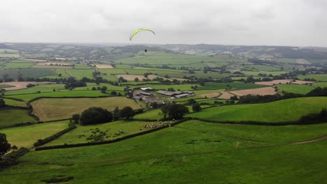 aerial shot following a paraglider flying above the devon countryside