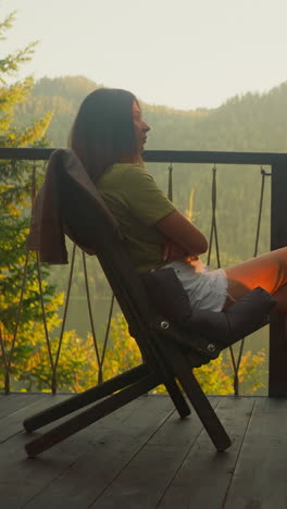 woman enjoys atmosphere of morning nature alone. relaxed woman sits in chair on terrace surrounded by calm summer forest watching environment