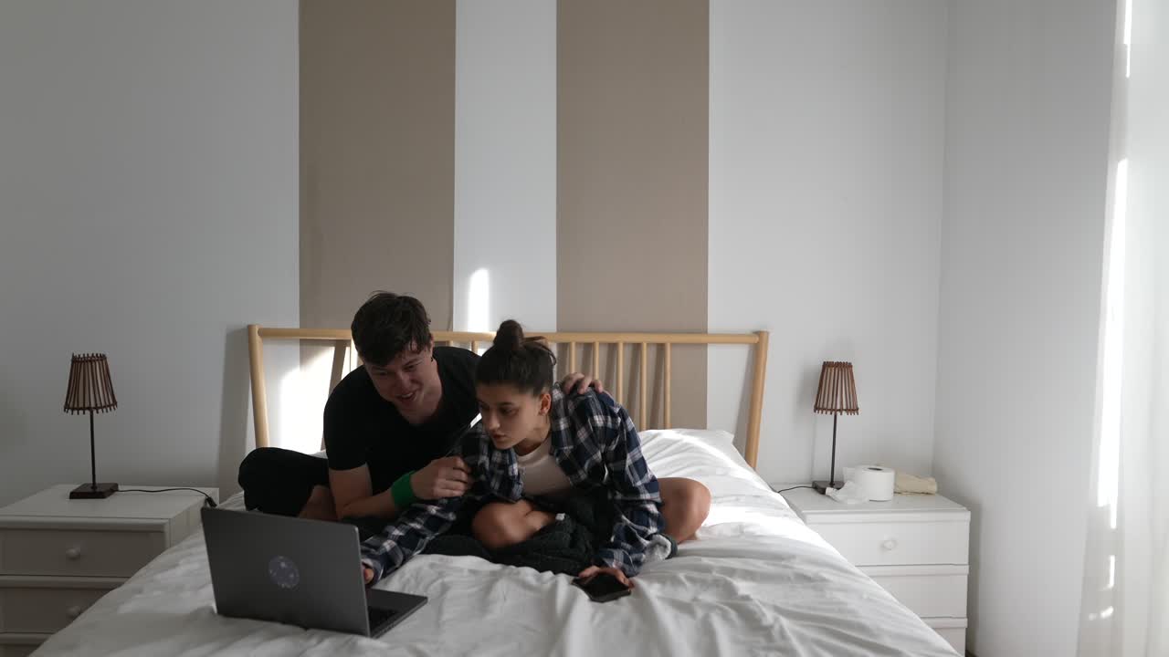 Couple relaxing on bed, using laptop and smartphone