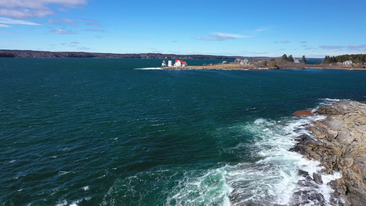 Sorvolando onde che si infrangono su un'isola rocciosa verso un faro in lontananza.