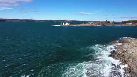 Flying-above-waves-crashing-on-a-rocky-island-towards-a-lighthouse-in-the-distance-AERIAL