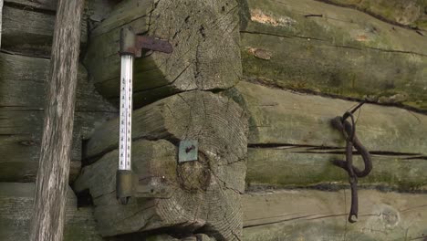 gorgeous close up view of an old vintage and rusty thermostat or thermometer on a decaying and mossy barn or shed log wooden wall outdoors. thermometer has measurments and number on it to show temp.