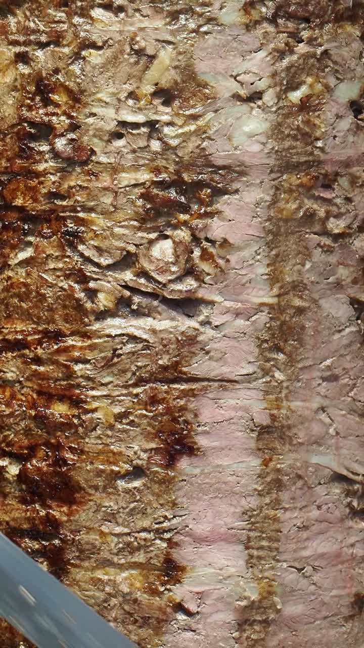Nærbillede af döner kebab-kød, der skæres fra en lodret grill