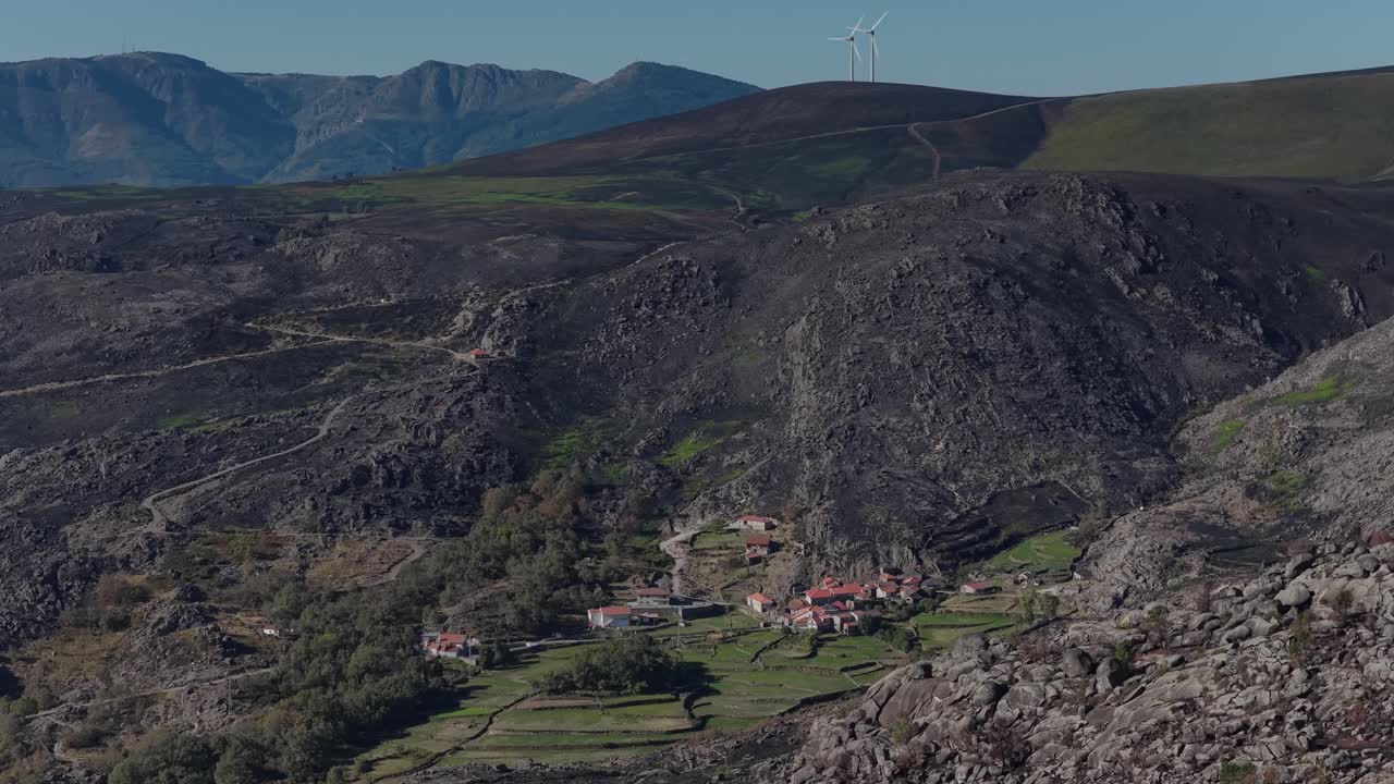 Green fields on a village with burnt landscape around it