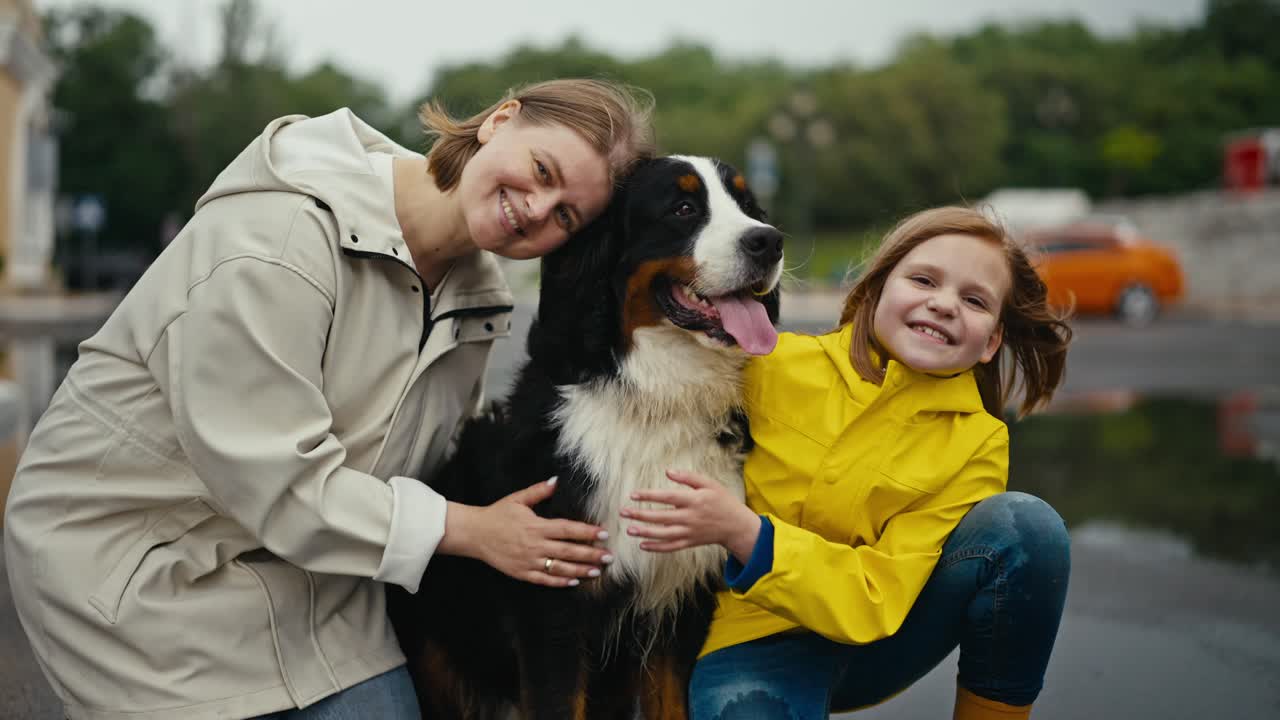 retrato de una feliz mujer rubia sentada con su hija adolescente acariciando a su perro de raza negra mientras caminaba en el parque después de la lluvia