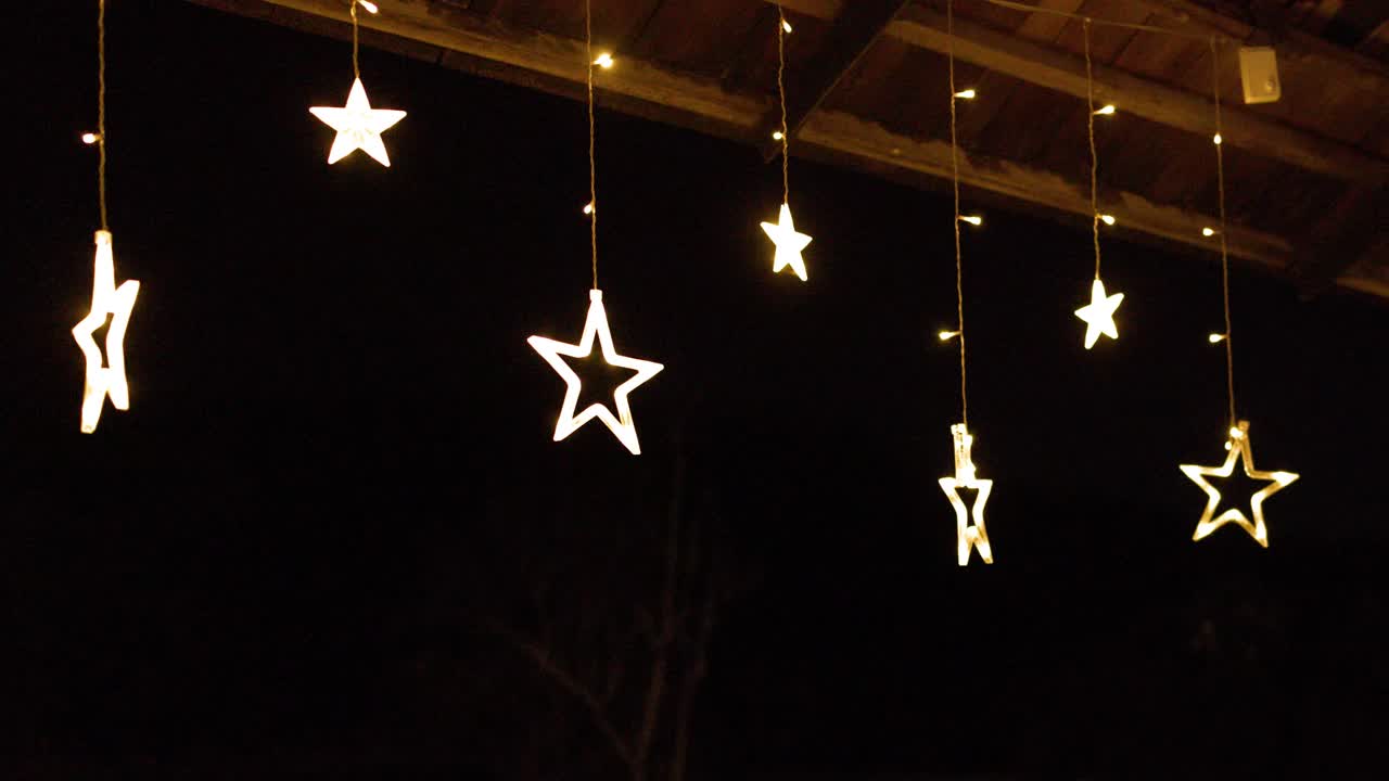 Warm star shaped string lights hang from a dark wooden terrace ceiling at night