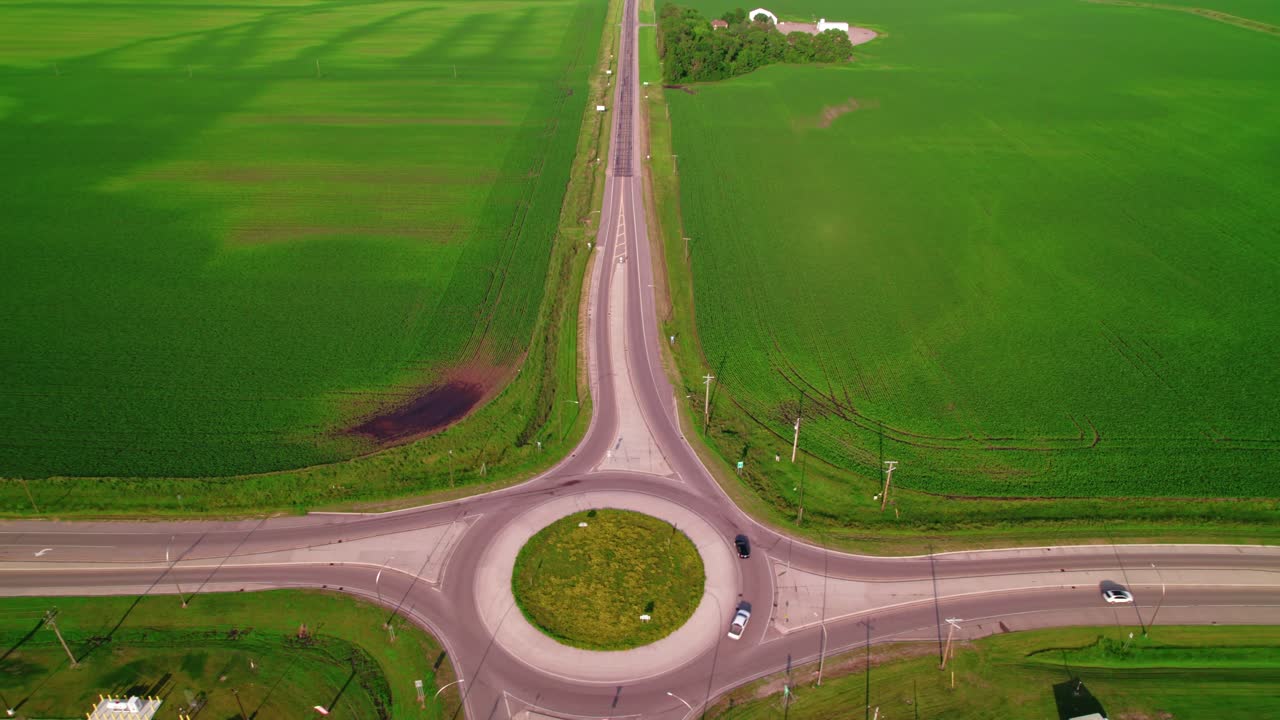Aerial shot of a hopper trailer truck approaching a roundabout in rural Minnesota, with vast green fields surrounding it.
