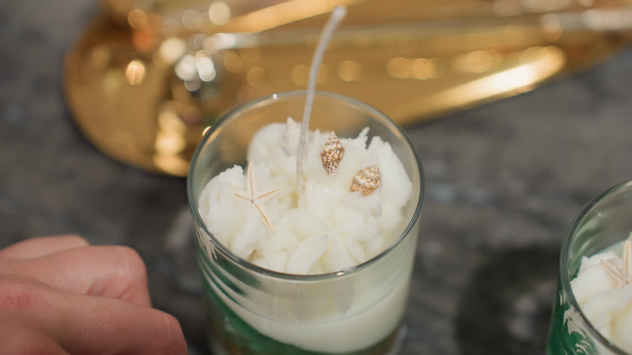 Culinary artist gently places white and golden shell atop creamy pipped icing sugar on decorated dessert in glass, showcasing attention to detail, elegant touch, and professional design